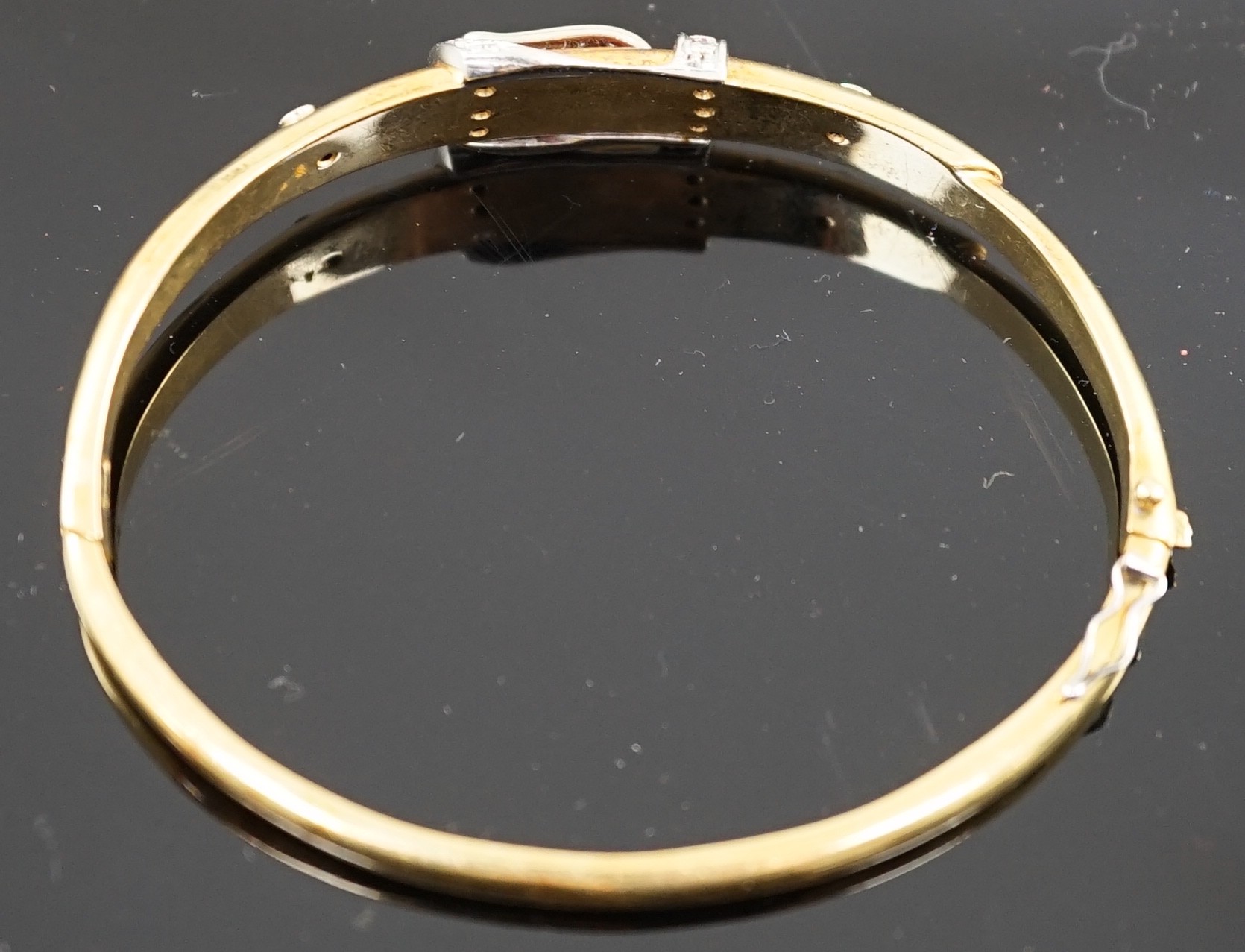 A gold and diamond set hinged bangle with central buckle motif